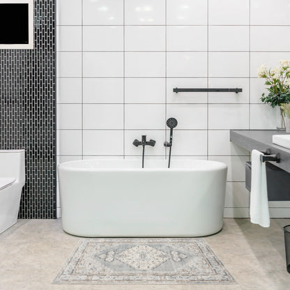 White freestanding oval bathtub with black fixtures in a modern tiled bathroom, featuring a black mosaic wall and vanity.