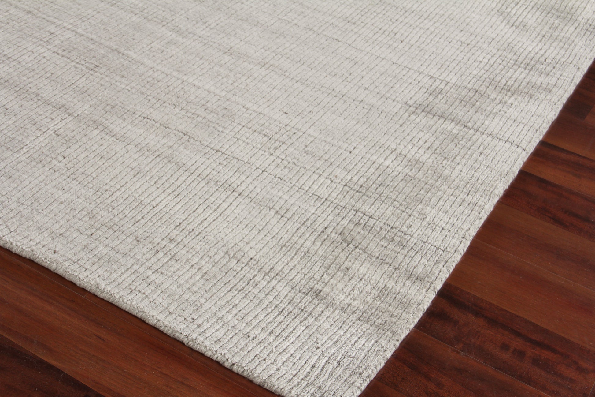 Beige textured flat-weave rug on dark hardwood floor; rectangular with subtle weave.