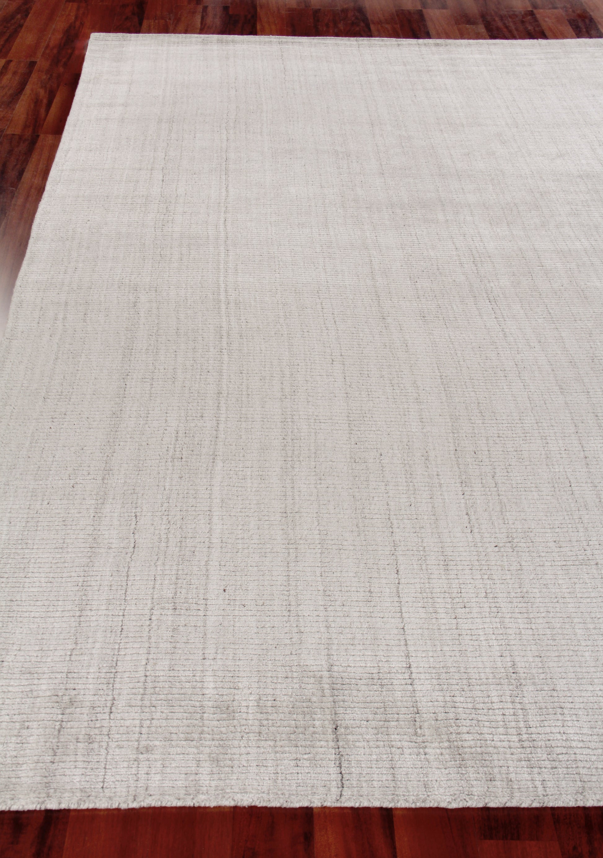 Cream flat-weave rug with subtle vertical stripe texture on dark hardwood floor.