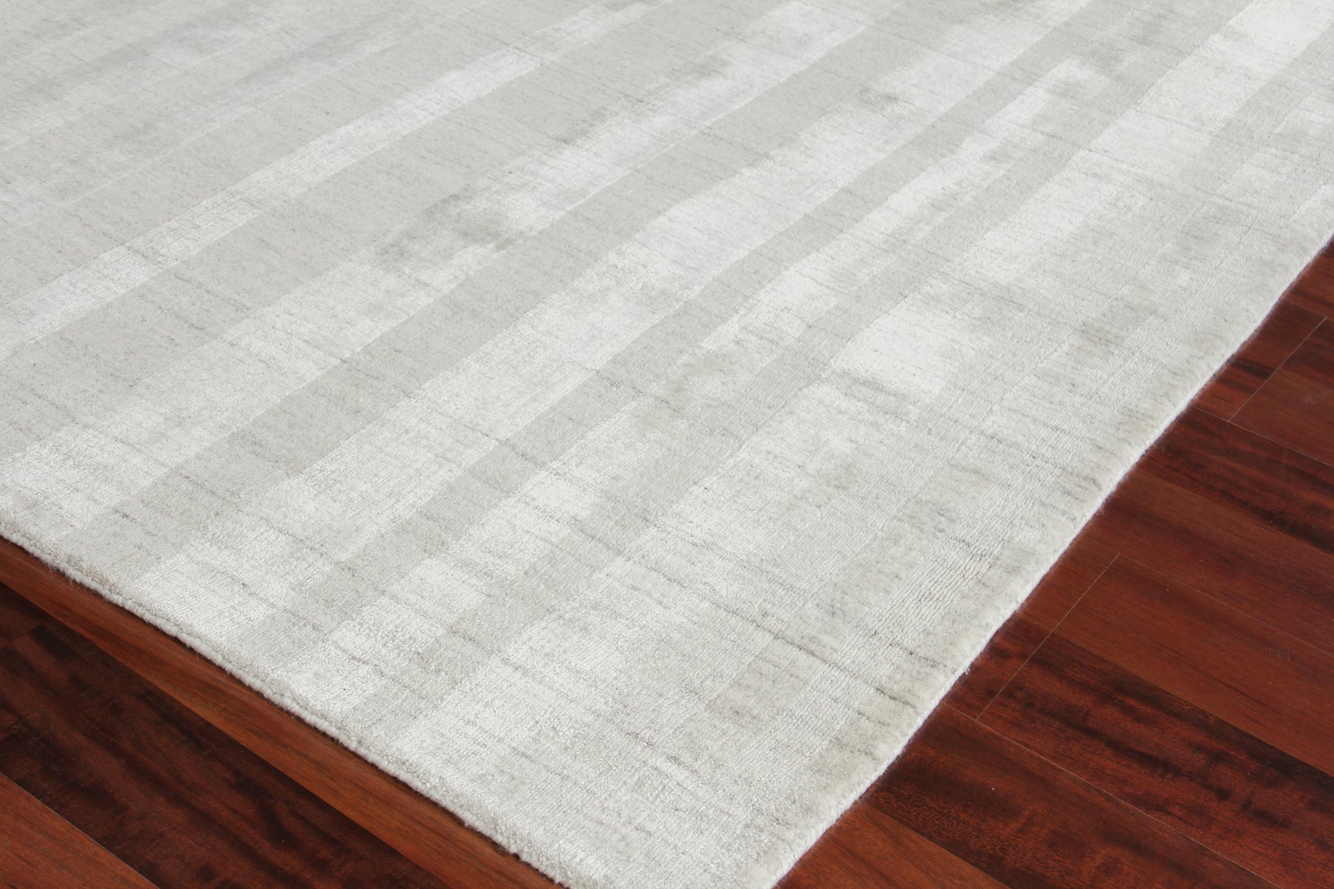 Soft light gray rectangular area rug with subtle striped pattern on dark hardwood floor.