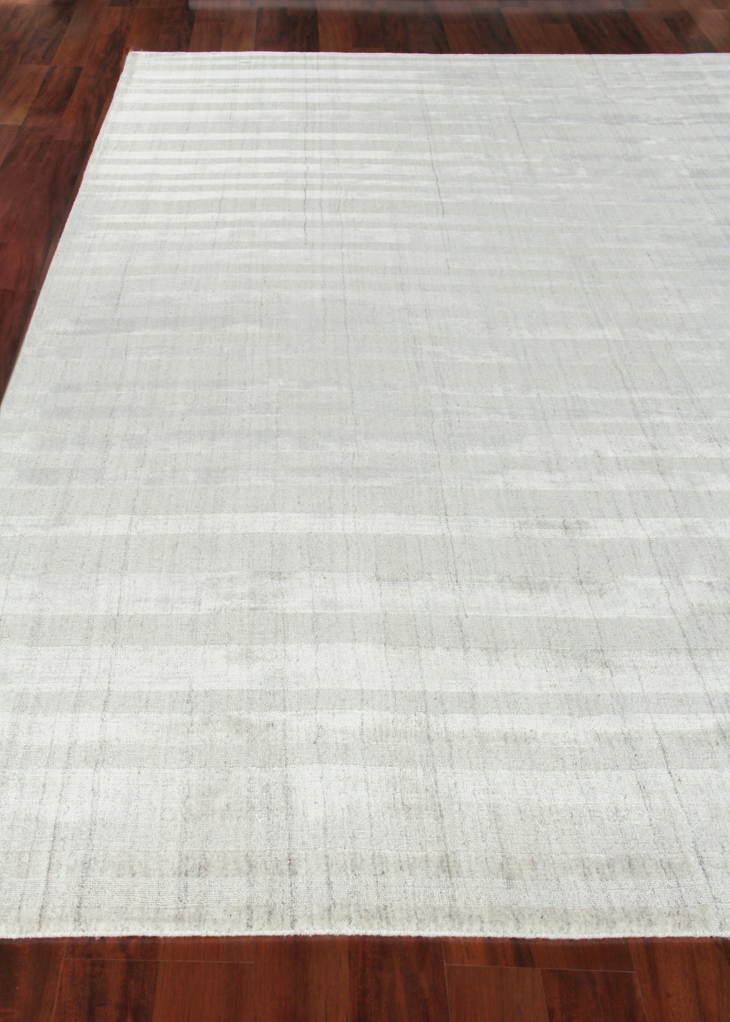 Light gray rectangular rug with subtle texture and soft horizontal stripes on dark wood floor.