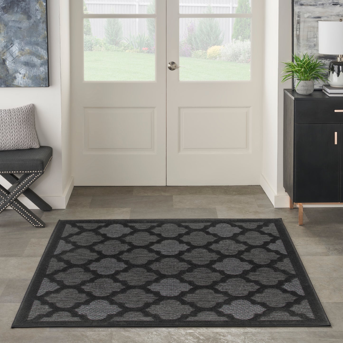 Rectangular charcoal-gray rug with a repeating trellis pattern and darker border in modern entryway.