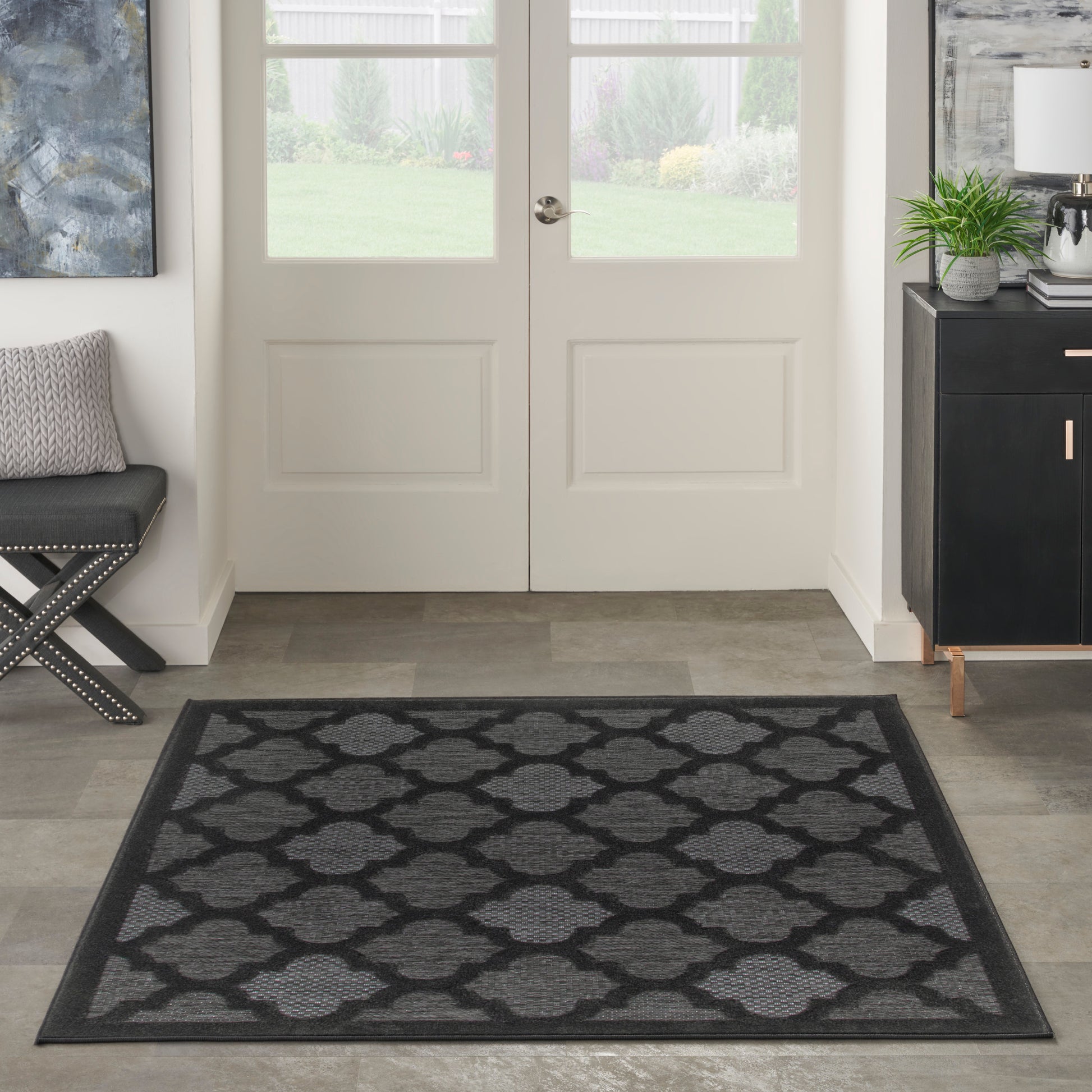 Rectangular charcoal-gray rug with a repeating trellis pattern and darker border in modern entryway.