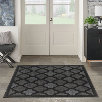 Rectangular charcoal-gray rug with a repeating trellis pattern and darker border in modern entryway.