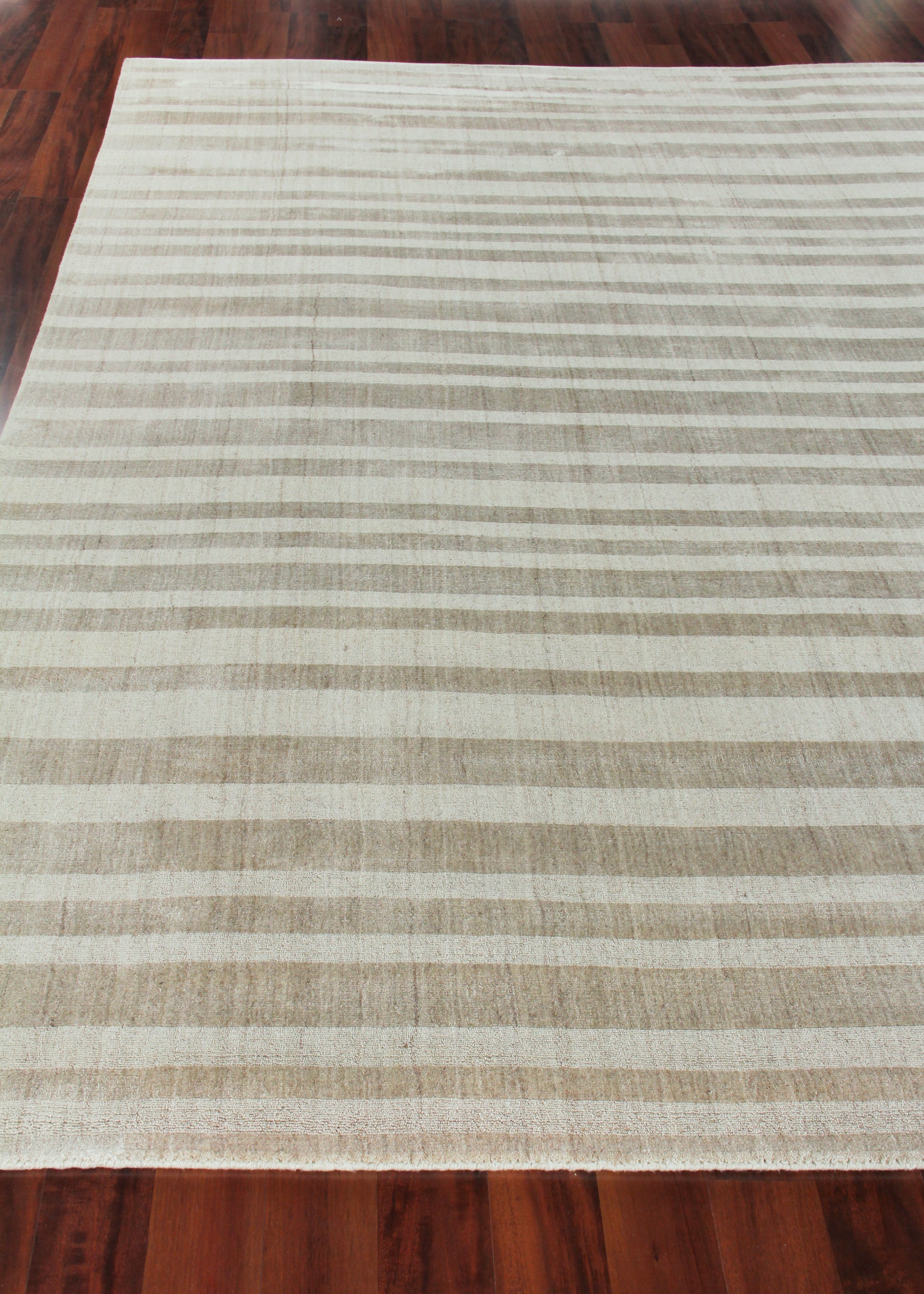 Cream and beige striped woven area rug on dark hardwood floor.