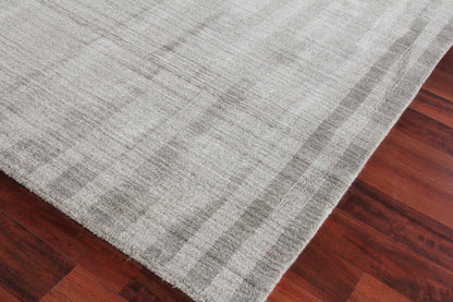 Light gray rug with subtle striped texture and soft pile laid over dark wooden floor.