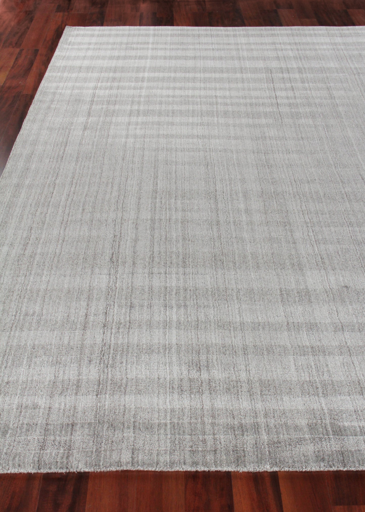 Rectangular light gray hand-loomed rug with subtle striped texture on dark hardwood floor.