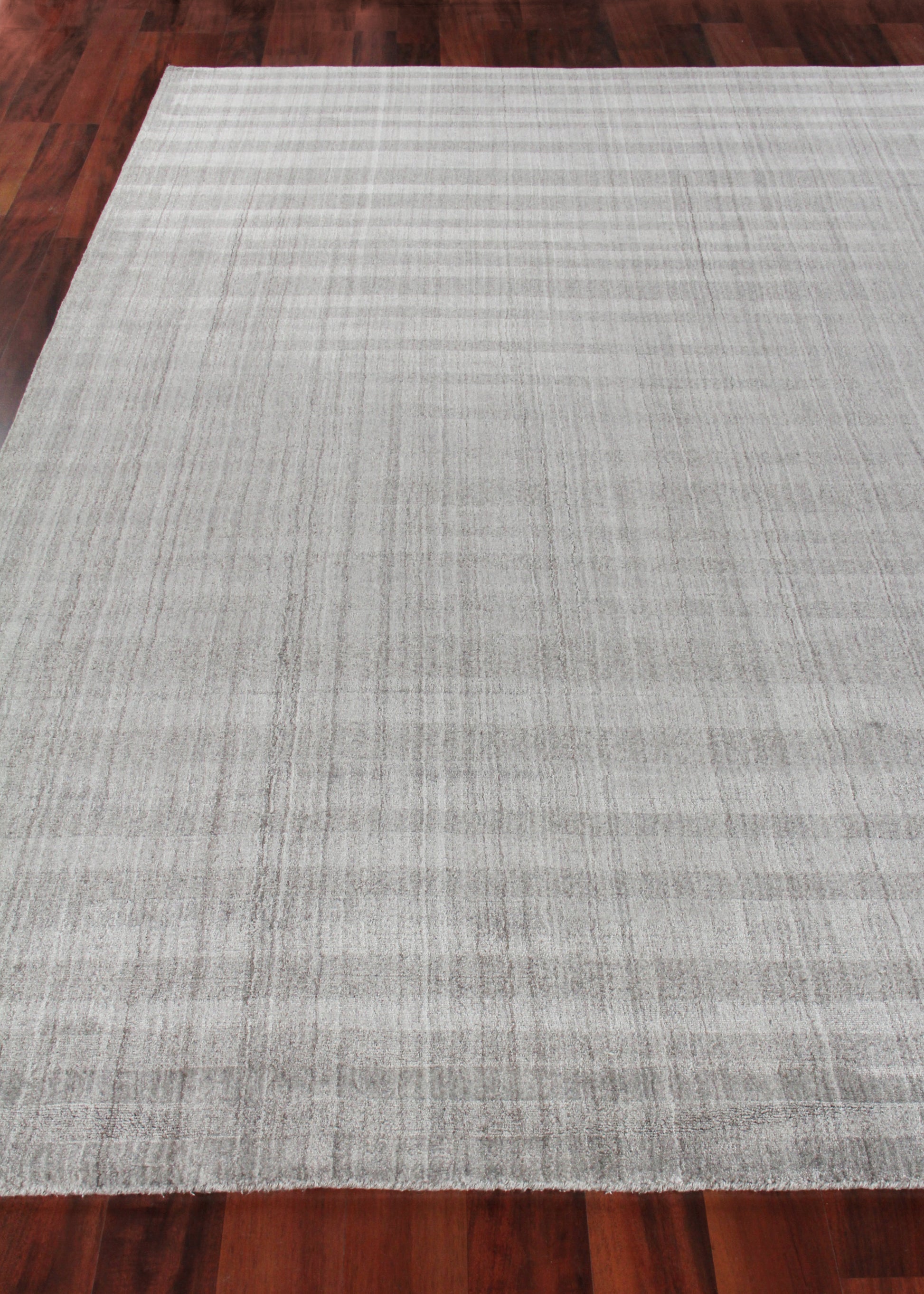 Rectangular light gray hand-loomed rug with subtle striped texture on dark hardwood floor.