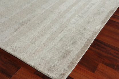 Cream-beige low-pile area rug with subtle striped texture on dark brown hardwood floor.
