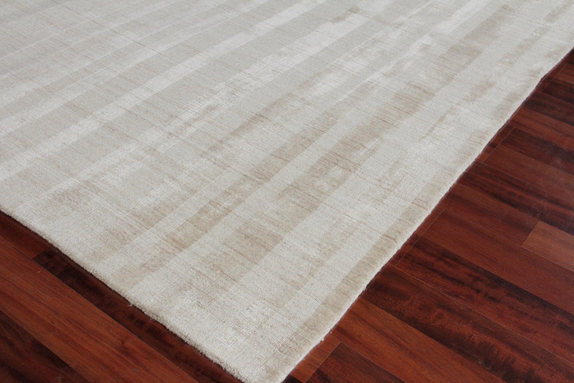 Cream-colored area rug with subtle striped pattern on dark hardwood floor.
