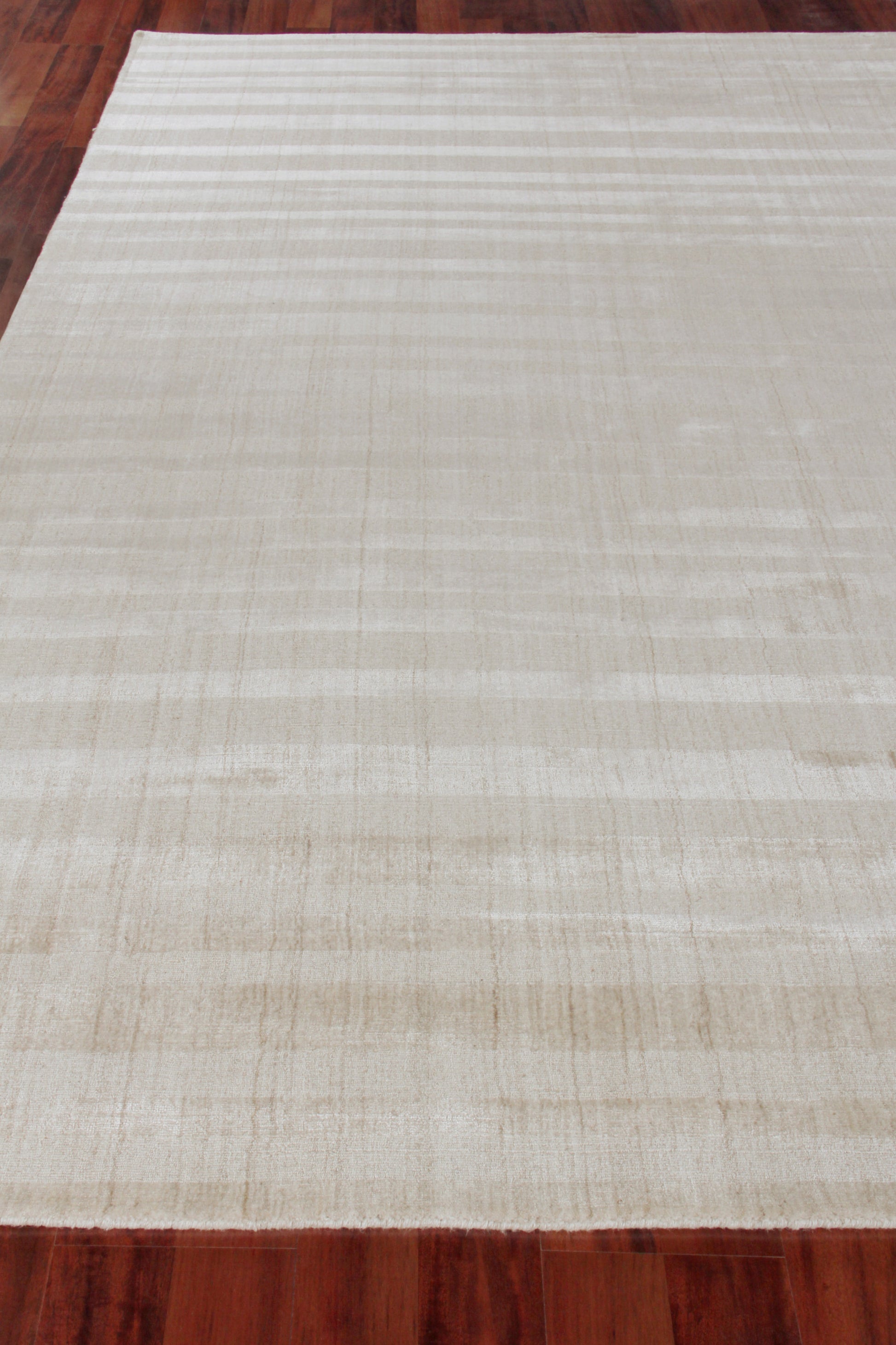 Cream hand-loomed rug with subtle tan stripes on a dark wooden floor.