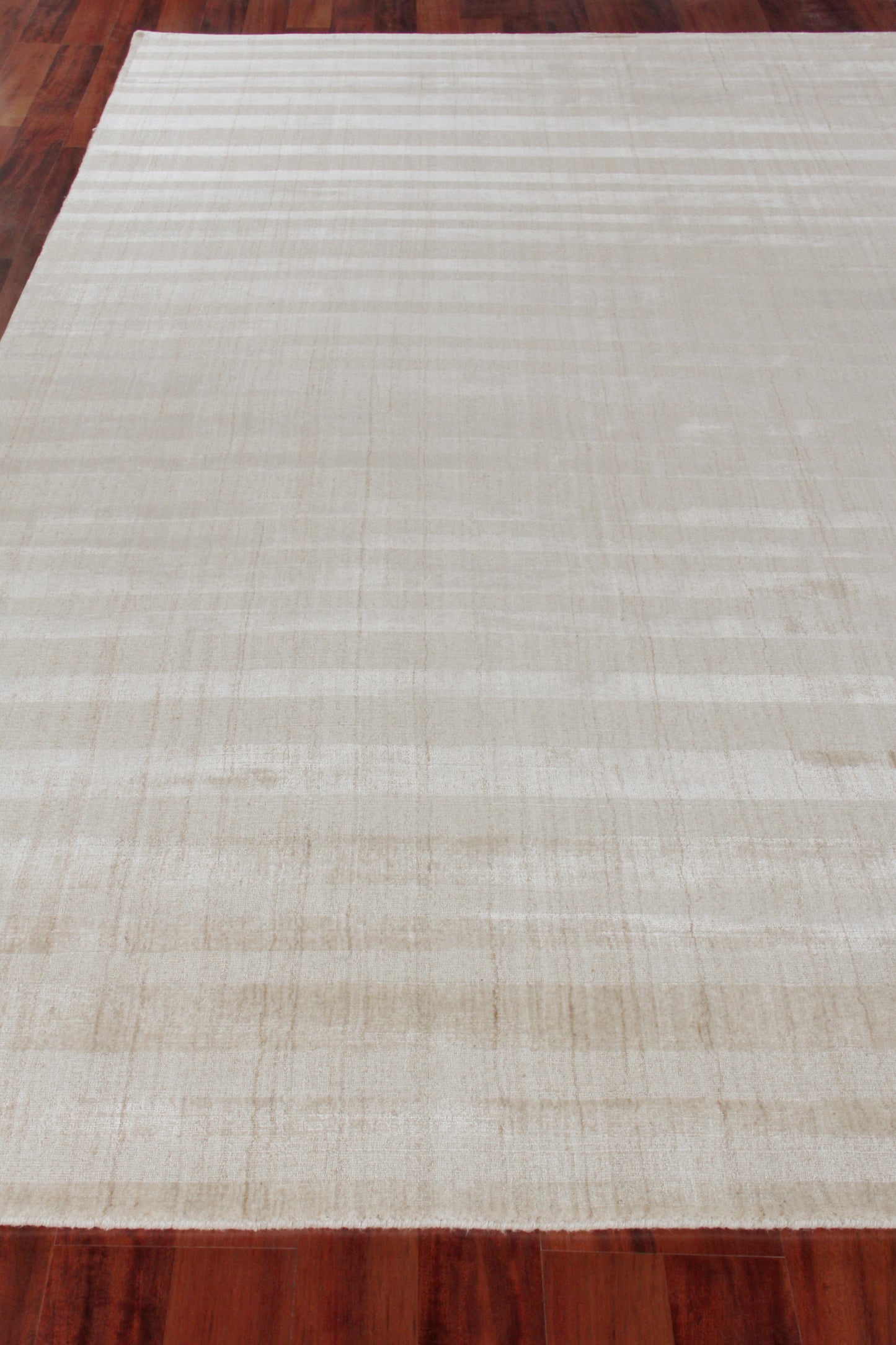 Cream-beige rectangular flat-weave rug with subtle striping on wood floor.