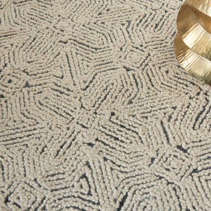 Beige loop-pile area rug with a dark geometric line pattern and a gold decorative piece in the corner.