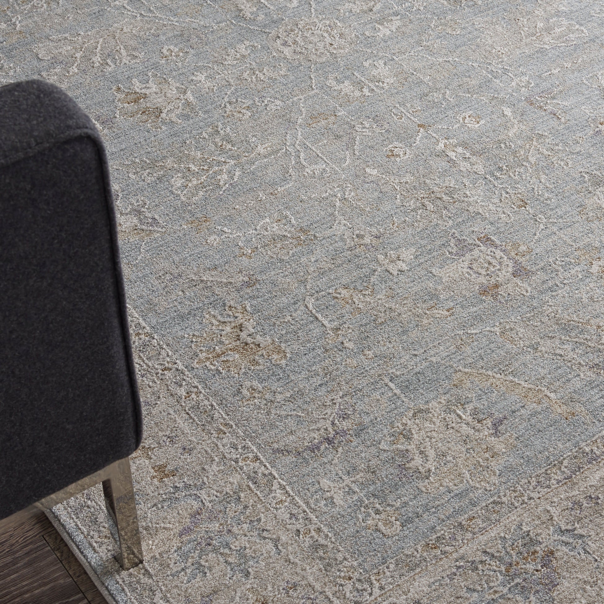 Dark gray upholstered chair with metal legs beside a light gray patterned rug featuring ornate floral medallions.