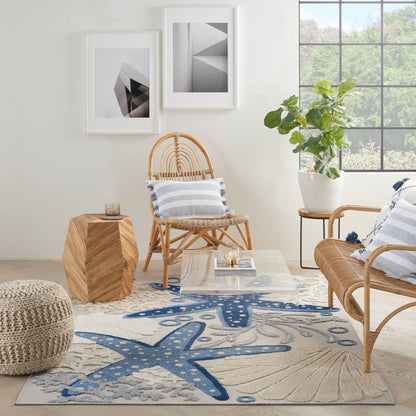 Bright living room with rattan chairs, striped cushions, glass coffee table, woven ottoman, blue starfish rug by the window.