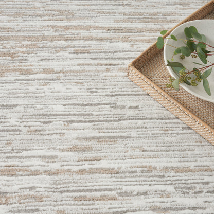 Beige and cream striped textured rug with a woven tray, white bowl, and eucalyptus.