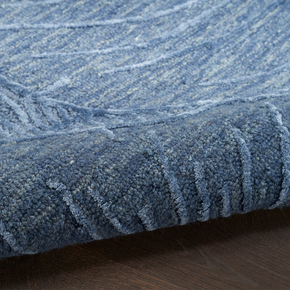 Blue textured area rug with a chunky loop pile and abstract lighter-blue pattern, rolled edge on a wooden floor.
