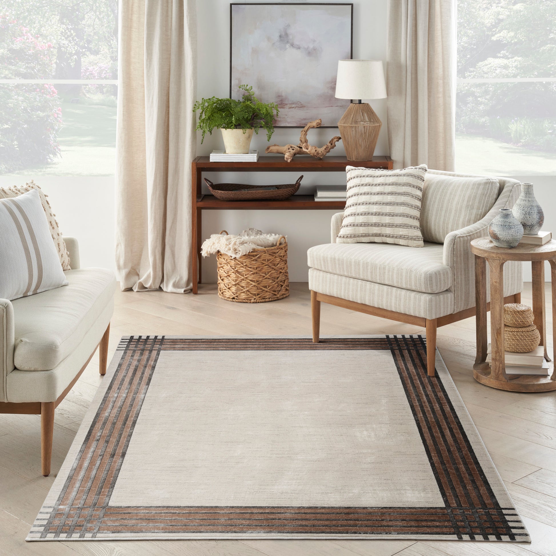 Bright neutral living room with light-striped chairs and a beige rug with brown/gray striped border; wood console and plants.