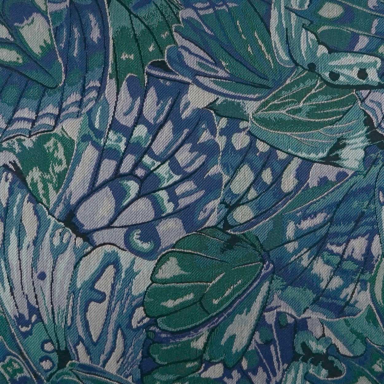 Close-up of tropical leaf fabric with blue, teal and green hues; bold botanical print, textile texture.