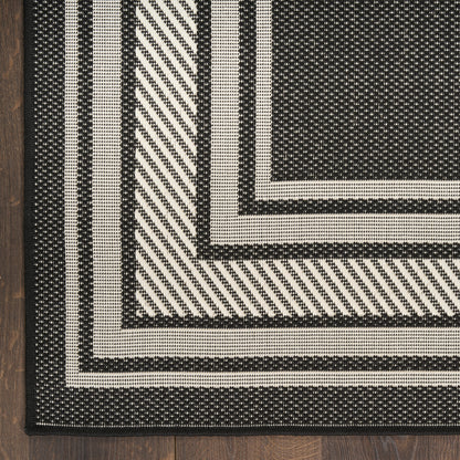 Monochrome black and ivory woven rug with concentric borders and diagonal striped accents on wood floor.