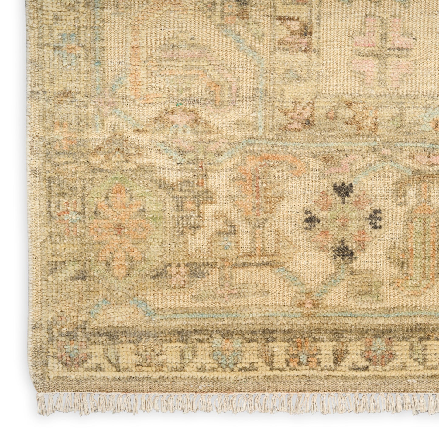 Close-up of a beige vintage Persian-style rug with muted blue and pink geometric motifs and fringe.