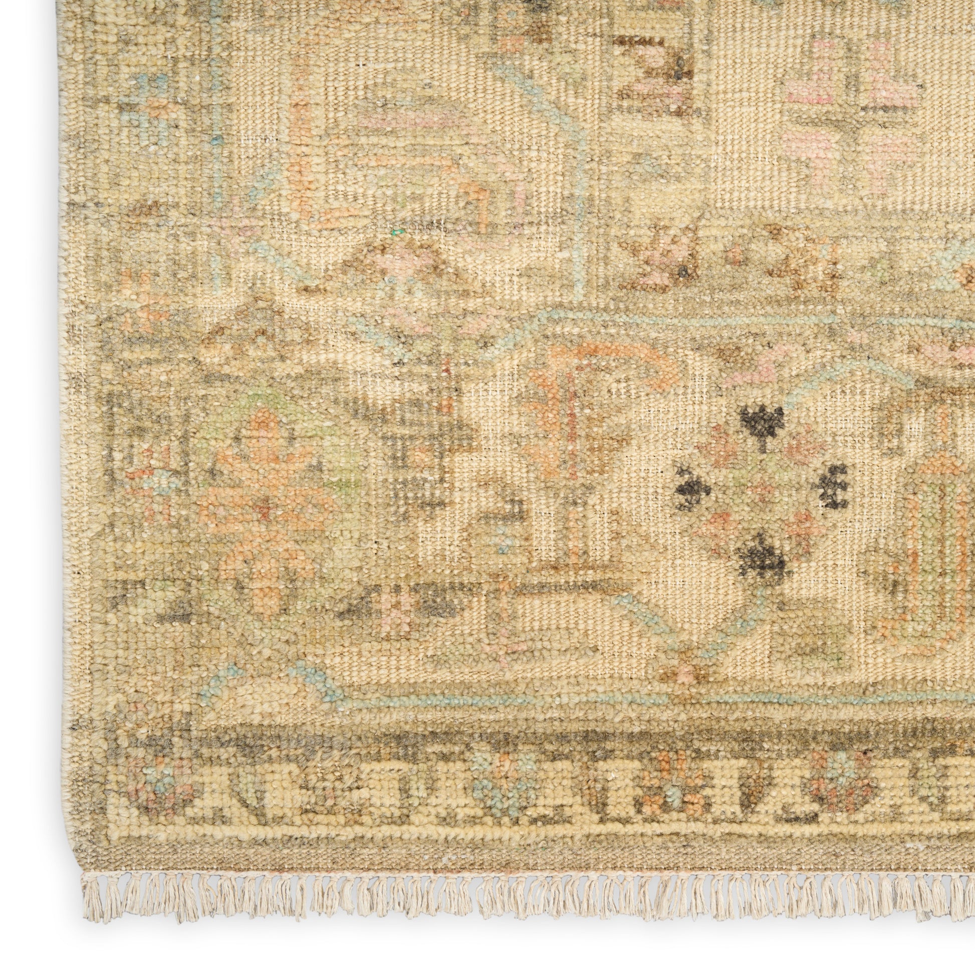Close-up of a beige vintage Persian-style rug with muted blue and pink geometric motifs and fringe.