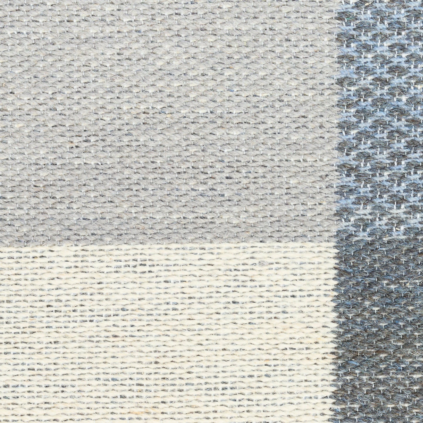 Close-up of a gray-beige woven rug with patchwork blocks and a dark gray textured border.