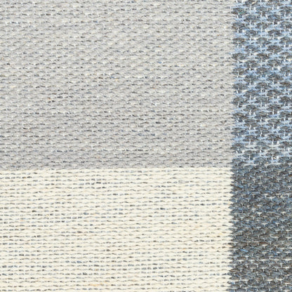 Close-up of a gray-beige woven rug with patchwork blocks and a dark gray textured border.
