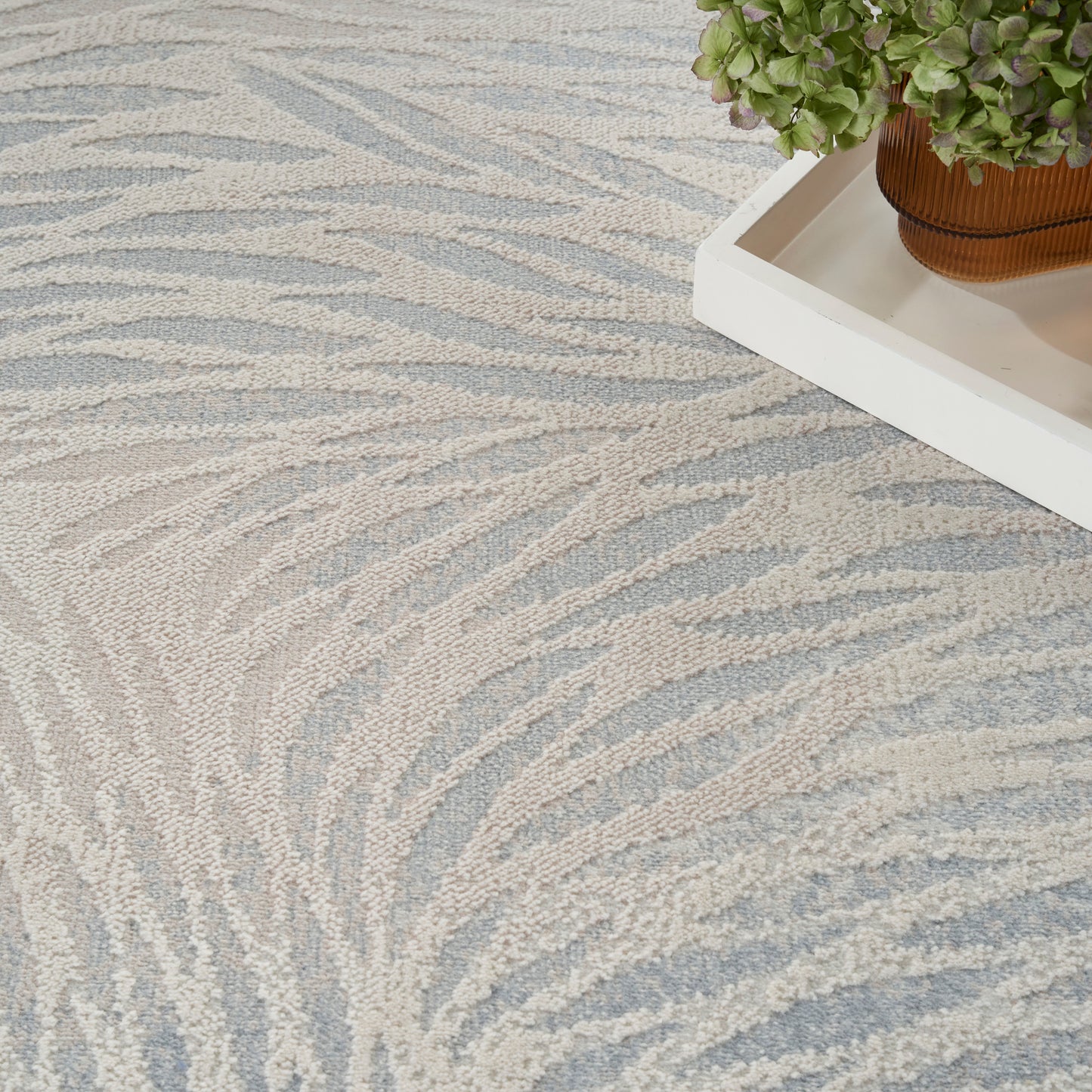 Light blue and beige zebra-pattern rug with a textured weave, beside a white tray holding a potted green plant.