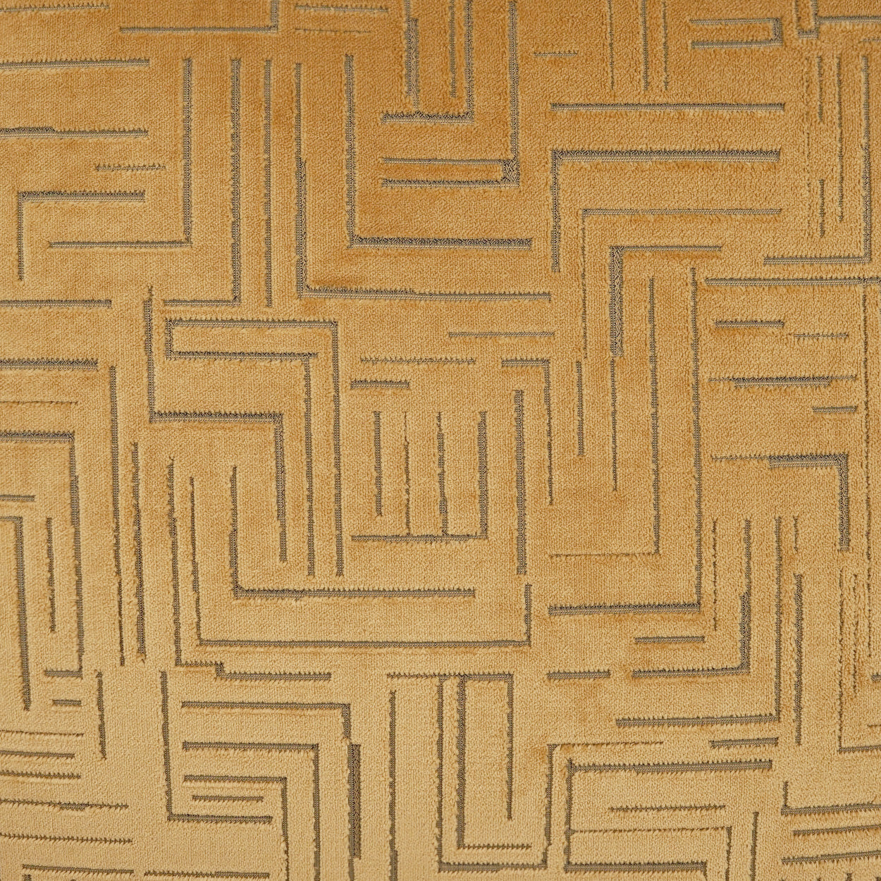 Gold-beige fabric with a geometric embossed maze pattern; textured upholstery or drapery material.
