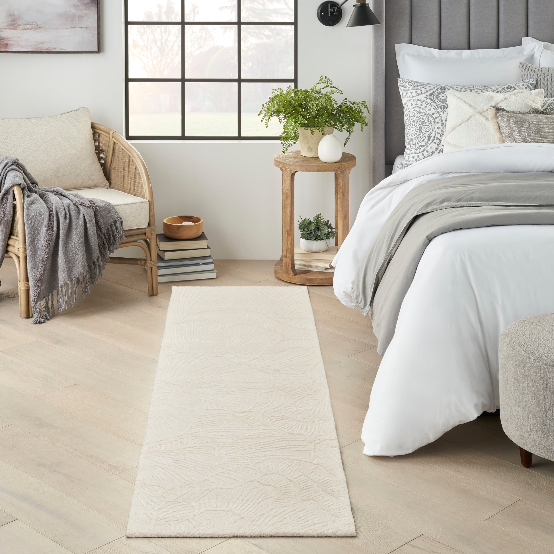 Cream textured rectangular rug runner in a tranquil neutral bedroom beside a bed and wicker chair.