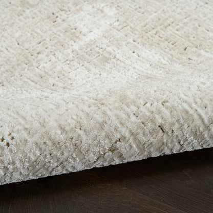 Beige textured rug with subtle geometric pattern, plush pile, folded edge on dark wood floor.