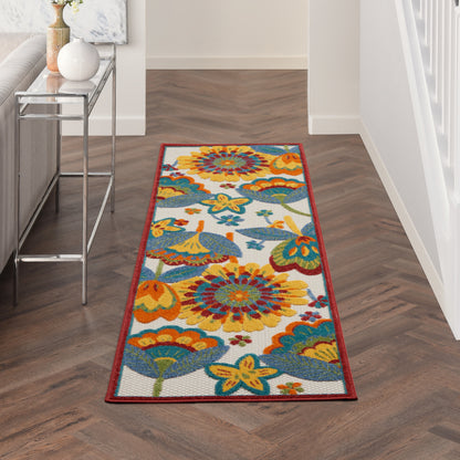 Long colorful floral runner rug with red border on herringbone wood floor in hallway beside glass console table.