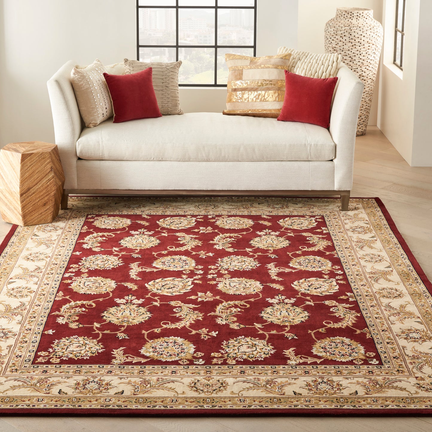 Cream sofa with red and beige cushions in a bright living room, centered on a burgundy oriental rug with beige and gold border.