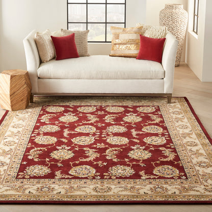 Cream sofa with red and beige cushions in a bright living room, centered on a burgundy oriental rug with beige and gold border.