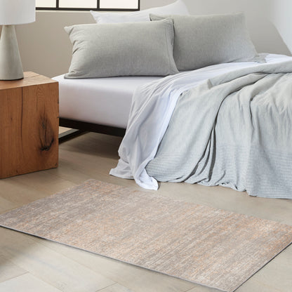 Soft gray bedding with white sheets and two gray pillows; wooden nightstand and beige-toned runner rug on pale wood floor.