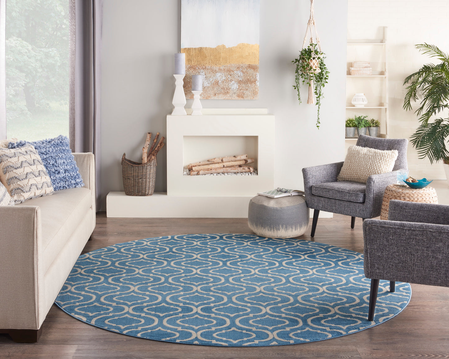 Round blue rug with white looping pattern in a light living room with beige sofa, gray chairs, and a fireplace.
