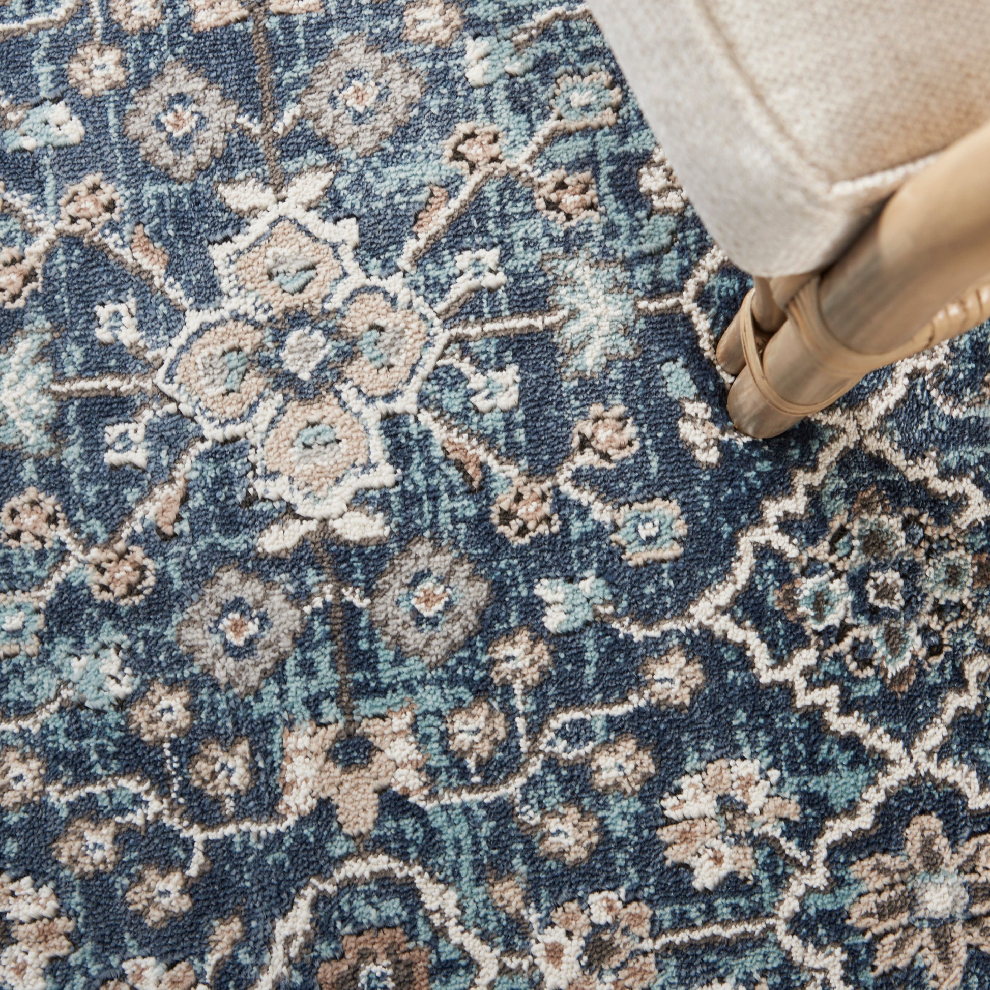 Blue and ivory floral rug in a Persian-style pattern; textured weave with beige accents, under a beige upholstered chair.
