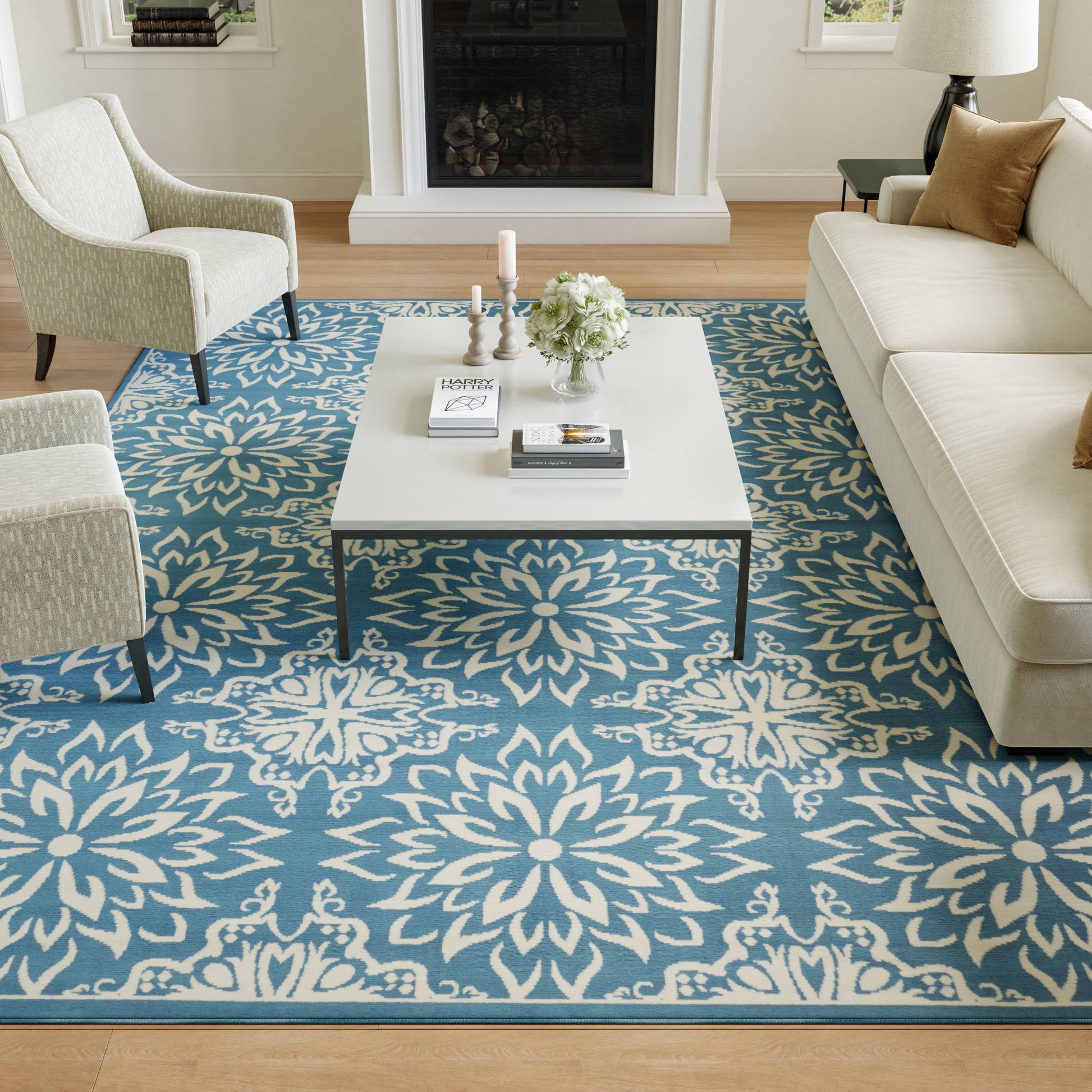 Cream upholstered chairs and sofa around a white coffee table on a blue floral-pattern rug in a modern living room.