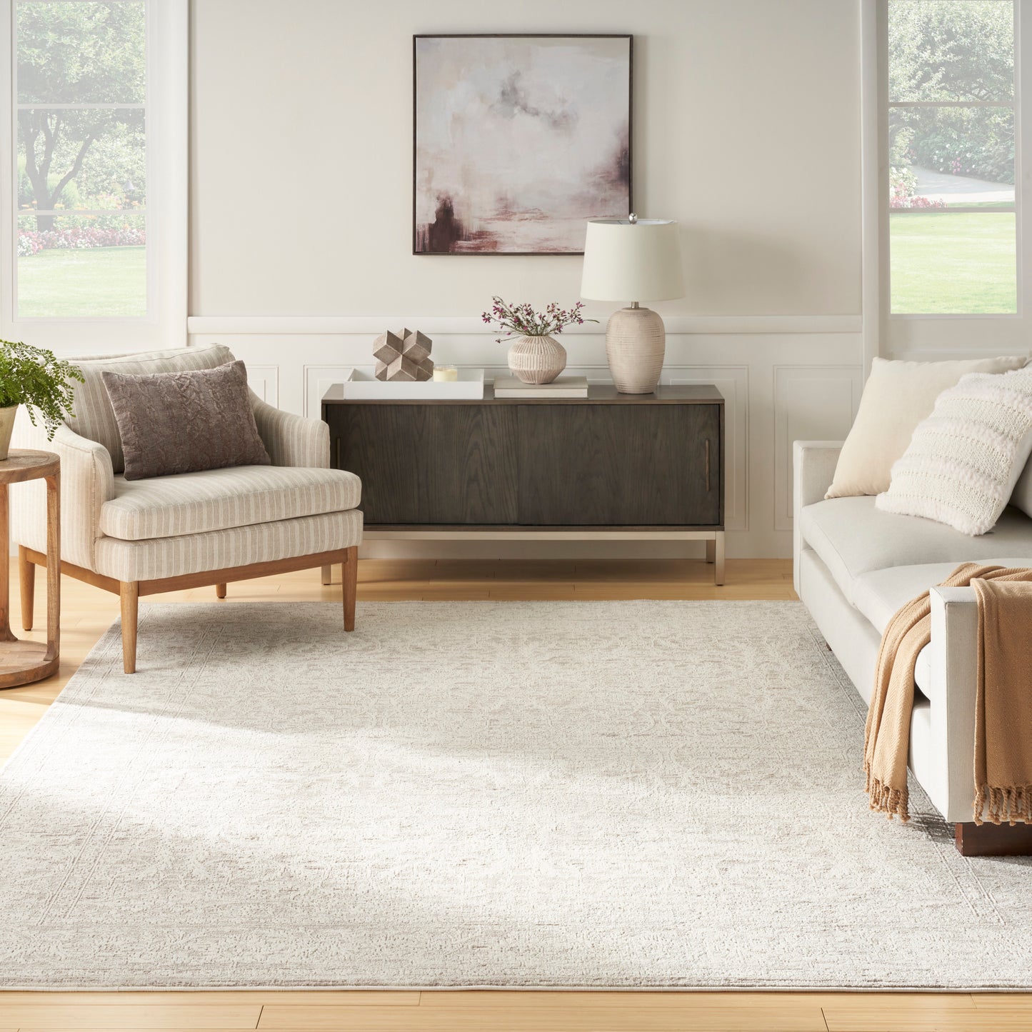 Neutral contemporary living room with beige walls, light sofa and armchair, dark wood console, beige rug, abstract art.