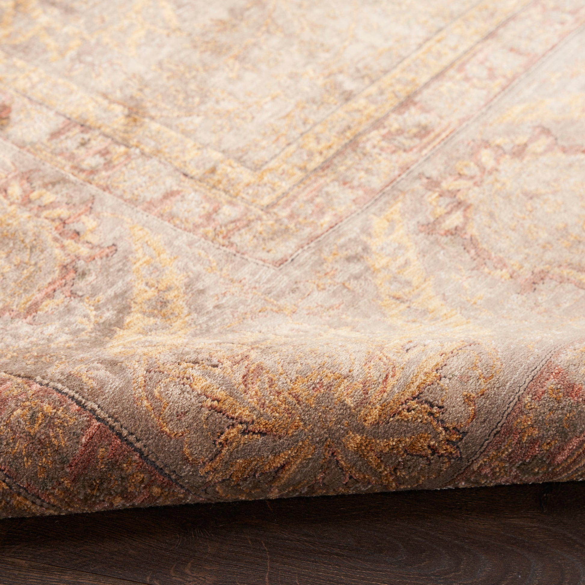 Corner of a soft vintage-style rug with pastel beige, pink and gold floral motifs on a wooden floor.