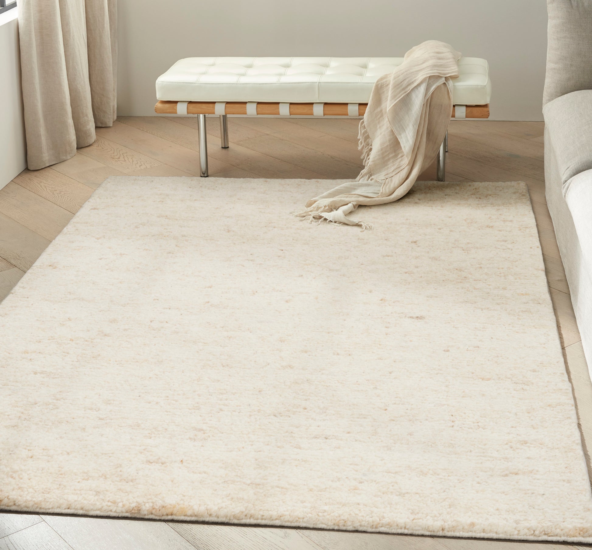 Cream plush area rug in a minimalist living room with a white tufted bench, beige throw, and light wood floor.