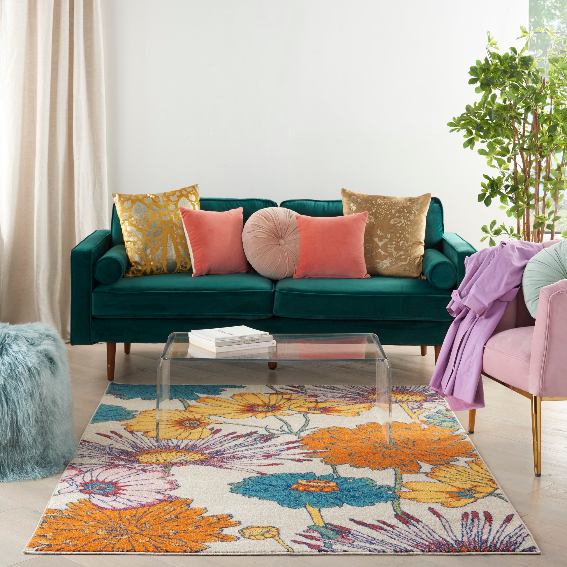 Teal velvet sofa with assorted cushions, glass coffee table, vibrant floral rug, pink chair with purple throw, potted plant.