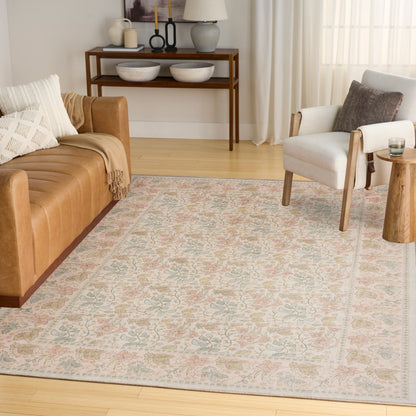 Living room with a pastel floral rug, tan leather sofa, light wood end table, and beige armchair with a gray cushion.
