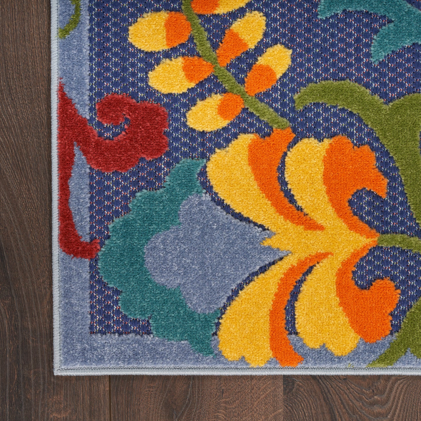 Outdoor colorful floral rug with blue background, yellow-orange petals, red accents, green leaves, and light blue border on floor