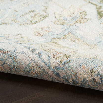 Close-up of plush pastel rug with blue, beige and sage green tones; folded edge on dark wood floor.