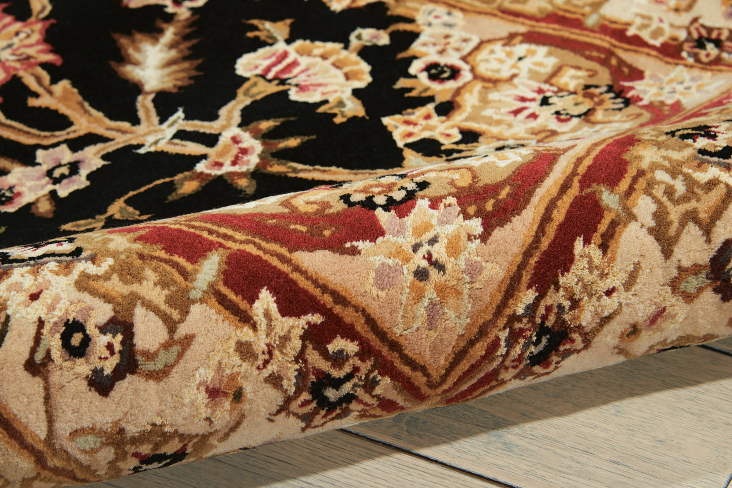 Traditional oriental rug with floral motifs in gold, red, and black; folded edge on light wood floor.