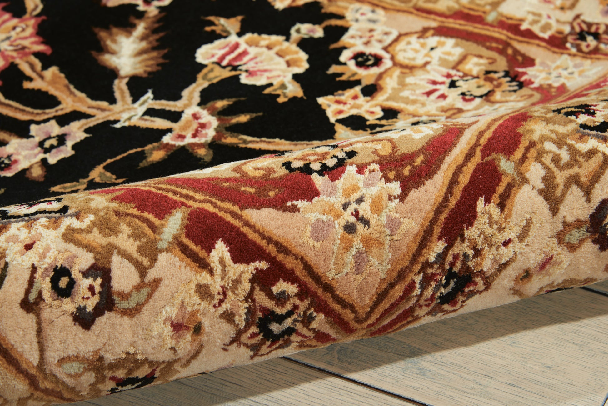 Traditional oriental rug with floral motifs in gold, red, and black; folded edge on light wood floor.