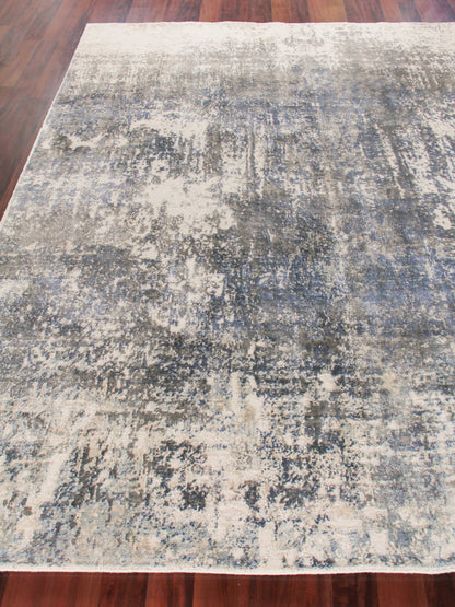 Abstract distressed area rug in blue, gray and ivory on a wooden floor; modern, plush texture.