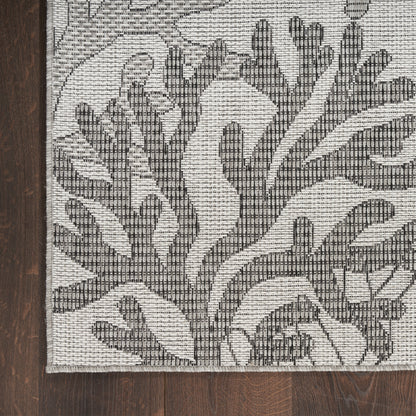 Rectangular cream and charcoal flat-weave rug with bold botanical pattern; modern neutral living room accent rug.